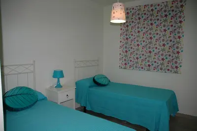 two beds in a room with blue sheets and a window at Apartamento Costa Ballena in Chipiona