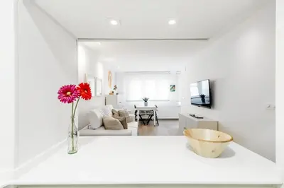 a white living room with a vase with a red flower at Casa Brasil - 1ª Linea Playa con Parking Incluido in Cádiz