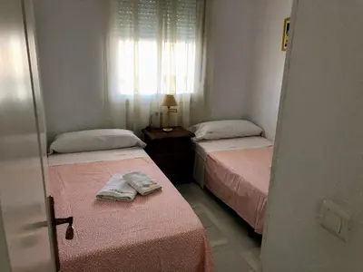 two beds in a room with pink sheets and a window at Apartamento Zinna in Chiclana de la Frontera