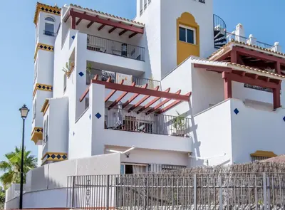 a white building with balconies and a fence at SibsSanlucar Piletas 1ª Linea Playa Piscina Terraza Padel Parking Wifi in Sanlúcar de Barrameda