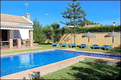 a swimming pool with blue chairs and a house at Casa Roche Viejo in Conil de la Frontera