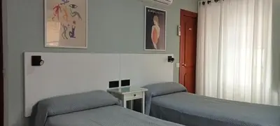 a bedroom with two beds and a table and a window at Hostal Bahía in Cádiz
