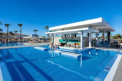 a pool at a resort with people sitting in the water at Hotel Riu Chiclana - All Inclusive in Chiclana de la Frontera