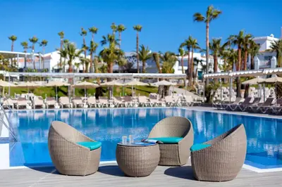 a pool at a resort with chairs and a table at Hotel Riu Chiclana - All Inclusive in Chiclana de la Frontera