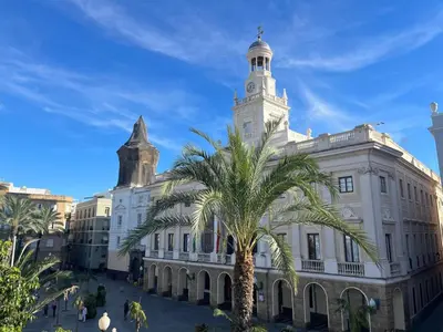 a building with a clock tower and a palm tree at El Chicuco en el corazón de Cádiz Grupo AC Gestion in Cádiz