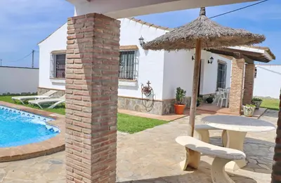 a patio with a table and an umbrella and a pool at Chalet de la casa Forestal in Conil de la Frontera
