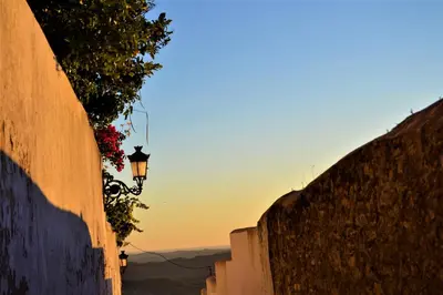 an alley with a street light with the sunset in the background at Casa La Muralla in Medina Sidonia