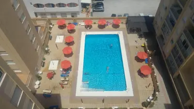 an overhead view of a swimming pool with red umbrellas at Apto Playa de Regla, primera linea, Parking, AA y wifi in Chipiona