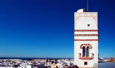 a tall white clock tower with a city in the background at No 38 Cádiz in Cádiz