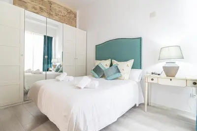a white bedroom with a white bed with a blue headboard at Allo Apartments Amargura I Centro Loft in Jerez de la Frontera