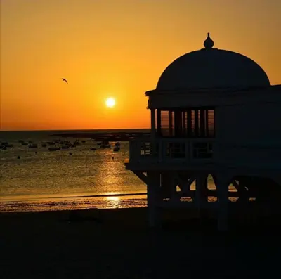 a building on the beach with the sunset in the background at Bonito piso in Puerto Real