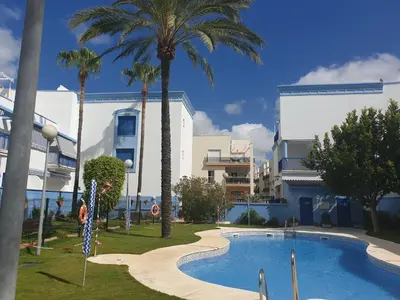 a swimming pool in front of a building with palm trees at Apartamento Vista Azul in Costa Ballena