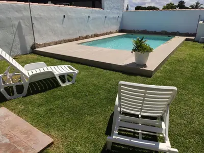two white chairs sitting on the grass near a swimming pool at Chalet Santi Playa de la Barrosa in Chiclana de la Frontera