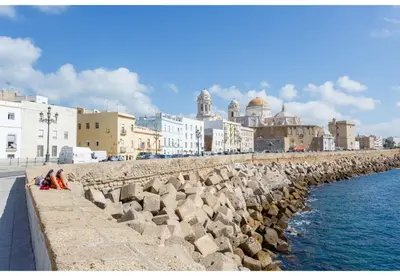 a group of people sitting on a wall next to the water at TERRAZA-Caleta Beach Home by Cadiz4Rentals in Cádiz