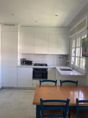 a kitchen with white cabinets and a wooden table at Apartamento La Barrosa, Chiclana in Chiclana de la Frontera