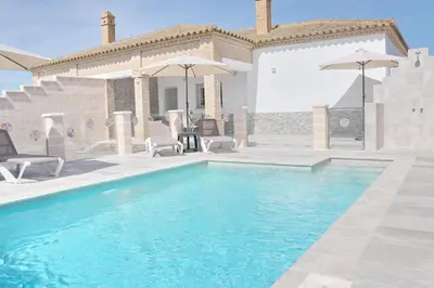 a pool with chairs and umbrellas in front of a house at Chalet Puente Tabla in Conil de la Frontera
