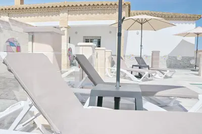 a row of lounge chairs and an umbrella on a patio at Chalet Puente Tabla in Conil de la Frontera