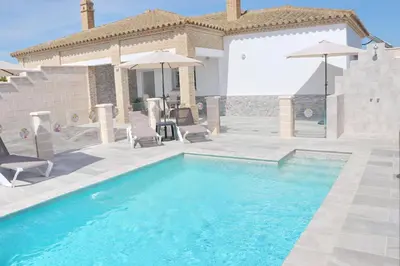 a swimming pool with chairs and umbrellas next to a house at Chalet Puente Tabla in Conil de la Frontera
