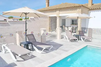 a group of chairs and umbrellas next to a pool at Chalet Puente Tabla in Conil de la Frontera