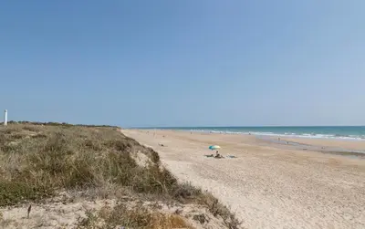 a beach with an umbrella and people on the beach at Casa Don Camilo Costa Ballena in Costa Ballena