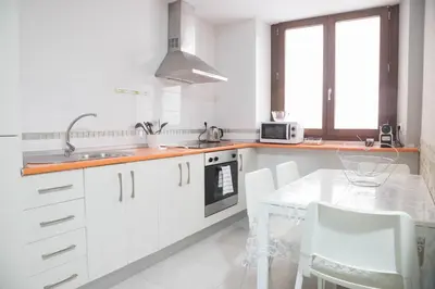 a white kitchen with white cabinets and a table at Apartamento Barrocal by Cadiz Time in Cádiz