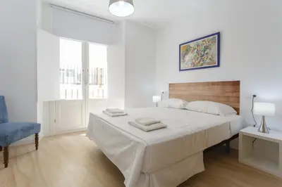 a white bedroom with a large bed and a chair at COLON15 Family Home by Cadiz4Rentals in Cádiz