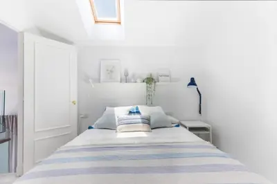 a white bedroom with a bed with blue and white pillows at Duplex Terraza Rivera Marisco 2 Dormitorios 2 Baños in El Puerto de Santa María