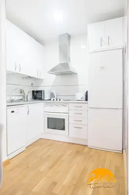 a white kitchen with white appliances and a wooden floor at Apartamento Caleta - FREE PARKING by Cadiz Time in Cádiz