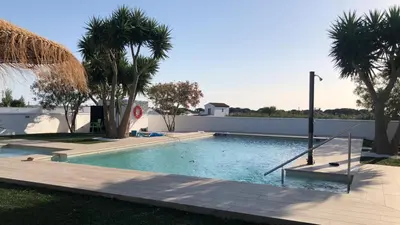 a swimming pool with palm trees and a fence at Villas Santa Ana in Conil de la Frontera