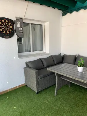 a patio with a couch and a table and a dartboard at ATICO LA ILUSION CON PARkING in Sanlúcar de Barrameda