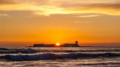 a sunset over the ocean with a lighthouse in the distance at Loft con Piscina ADULTS ONLY in Chiclana de la Frontera