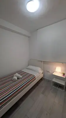 a white bedroom with a bed and a night stand at Playa y Sol Grupo AC Gestion in Cádiz