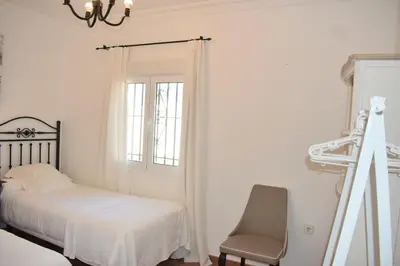 a bedroom with a bed and a chair and a window at Villa María Elena, en Fuente del Gallo in Conil de la Frontera