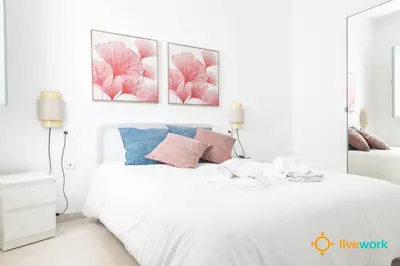 a bedroom with a white bed with four pictures on the wall at Apartamento Floral by LiveWork in Cádiz
