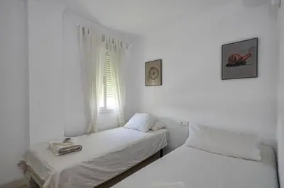 two beds in a white room with a window at Barrosa Frente al Mar in Chiclana de la Frontera