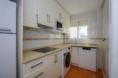 a kitchen with white cabinets and a sink and a dishwasher at Barrosa Frente al Mar in Chiclana de la Frontera