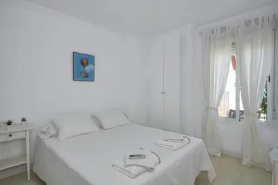 a white bedroom with a bed and a window at Barrosa Frente al Mar in Chiclana de la Frontera