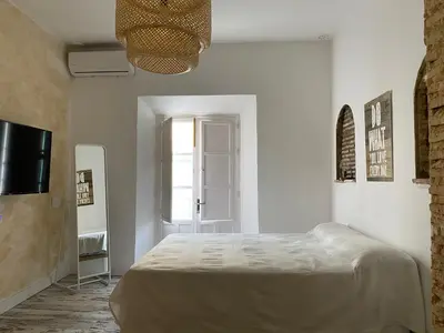 a white bedroom with a bed and a television at LA CUEVA DEL LOCO, Bretones 29 in Sanlúcar de Barrameda