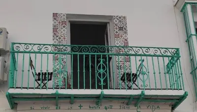 a balcony with a green railing on a building at LA CUEVA DEL LOCO, Bretones 29 in Sanlúcar de Barrameda