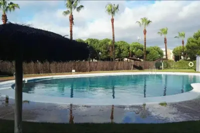 a swimming pool with palm trees and a fence at Precioso apartamento muy cerca de la playa in Chiclana de la Frontera