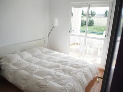 a white bed in a room with a large window at Flamingo Golf B in Sanlúcar de Barrameda