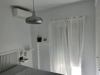 a white bedroom with a bed and a window at Apartamento Campoamor in Sanlúcar de Barrameda