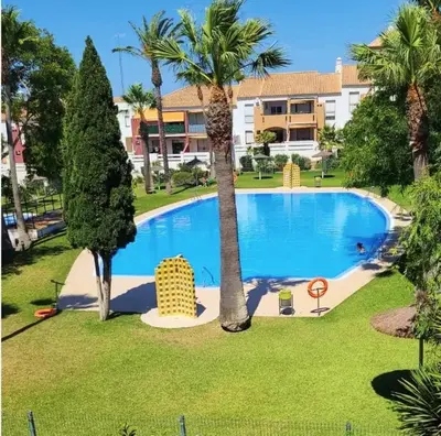 a large swimming pool with palm trees and a building at Cozy Chalet - playa a 200m in Chiclana de la Frontera
