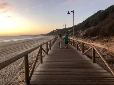 two people walking down a boardwalk on the beach at 'Sweet home' Loft con piscina en la mejor playa de El Puerto in El Puerto de Santa María