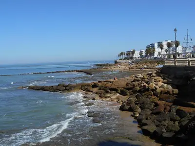 a beach with rocks and the ocean and palm trees at 300-Meter-bis-zum-Strand-Caracola-Wohnung-mit-Garten in Chipiona
