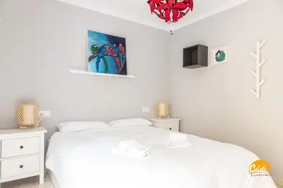 a white bedroom with a bed and a painting on the wall at Casa Arcoiris by Cadiz Time in Cádiz