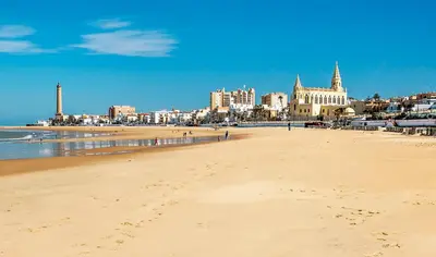 a sandy beach with a city in the background at Hotel Vértice Chipiona Mar in Chipiona