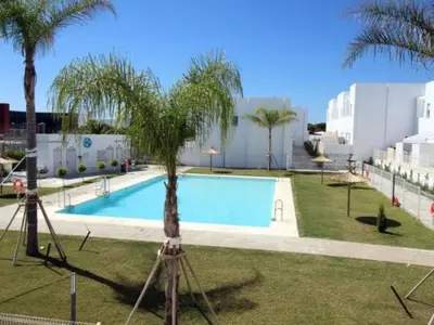 a pool with a palm tree next to a building at La Fontanilla Place in Conil de la Frontera