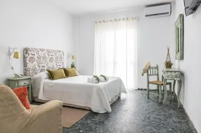 a white bedroom with a bed and a chair at Hotel Marhava in Conil de la Frontera