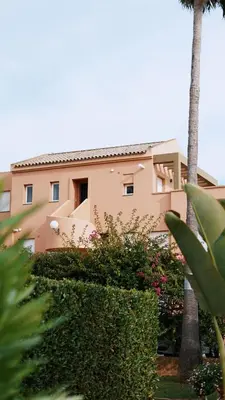 a building with a palm tree and some bushes at Jardín del Golf Nº 36 by Fontanilla del Mar Holidays Rentals in Chiclana de la Frontera
